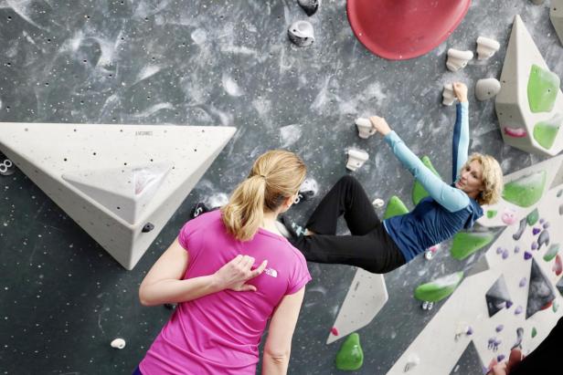 Eine Frau sichert eine andere beim Bouldern in einer Kletterhalle.