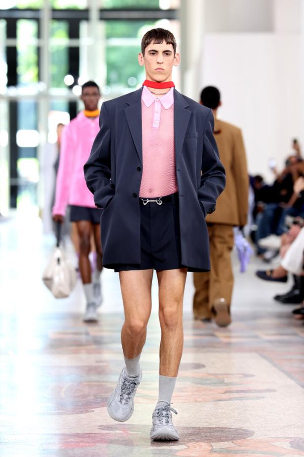 Ein Mann in Shorts, Blazer und Turnschuhen läuft auf einem Laufsteg.