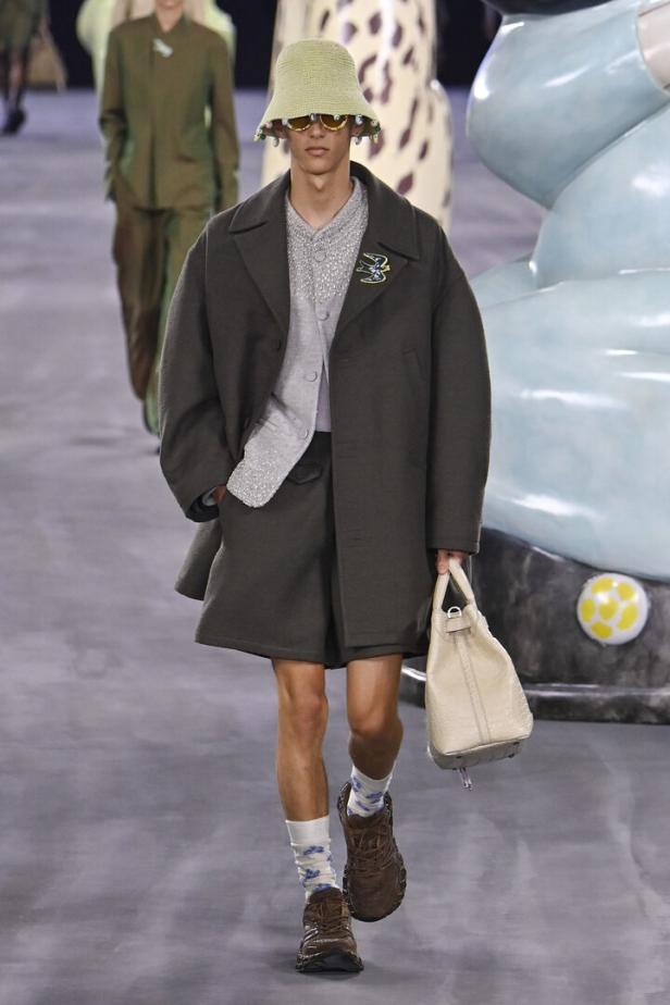 Ein Mann in Shorts, Mantel und Fischerhut läuft auf einem Laufsteg.