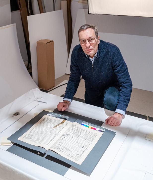 Ein Mann beugt sich über eine geöffnete Partitur in einem Archivraum.