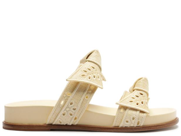 Ein Paar beigefarbene Sandalen mit Schleifen und Lochmuster stehen auf einem weißen Hintergrund.