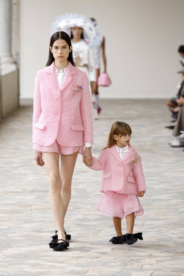 Ein Model und ein kleines Mädchen in passenden rosa Anzügen laufen Händchen haltend über einen Laufsteg.