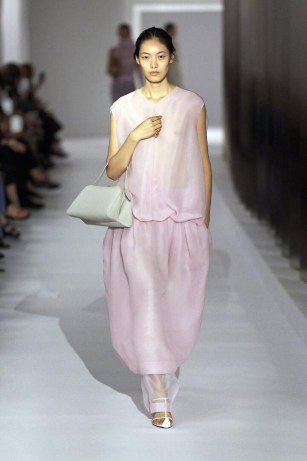 Eine Frau in einem rosa Kleid mit einer hellblauen Handtasche auf einem Laufsteg.