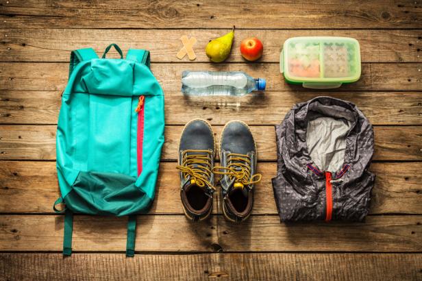 Ein Rucksack, Schuhe, eine Jacke, Essen und Trinken liegen auf einem Holztisch.