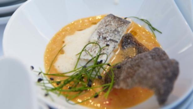 Ein Teller mit Fisch, Sauce und Kräutern wird serviert.