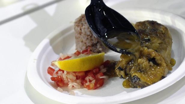 Mit einem Löffel wird Soße über ein Gericht mit Reis, Salat und Zitrone gegeben.