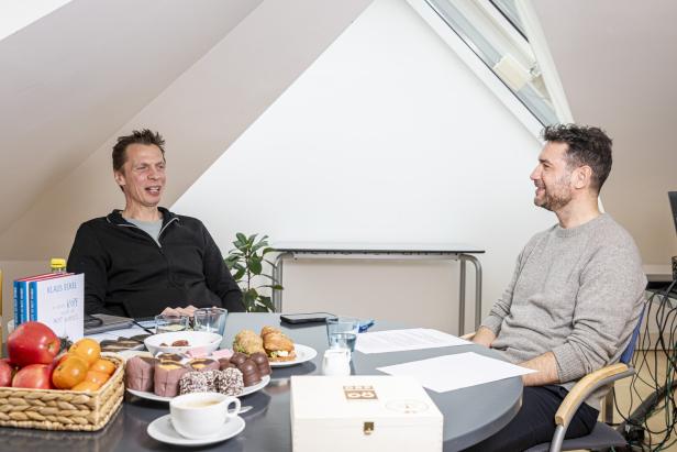 Zwei Männer sitzen an einem Tisch mit Essen und Getränken und unterhalten sich.