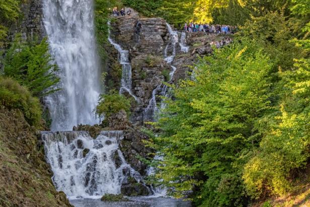 Ein großer Wasserfall inmitten eines dichten Waldes, umgeben von üppigem Grün und natürlichen Felsen.