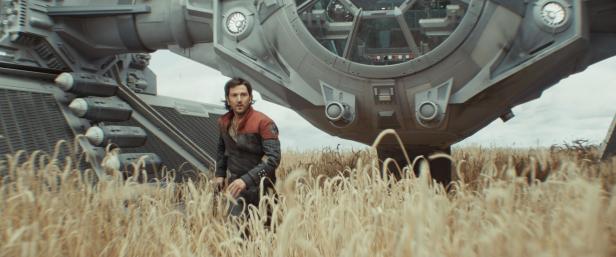 Diego Luna steht vor einem TIE-Jäger in einem Feld.