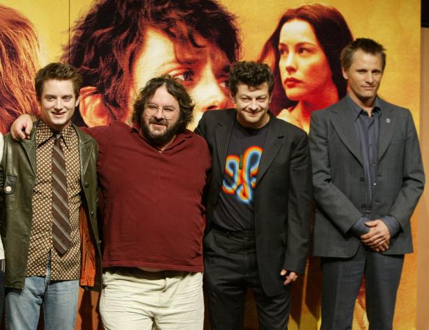 Elijah Wood, Peter Jackson, Andy Serkis und Viggo Mortensen posieren vor einem Poster für „Der Herr der Ringe“.