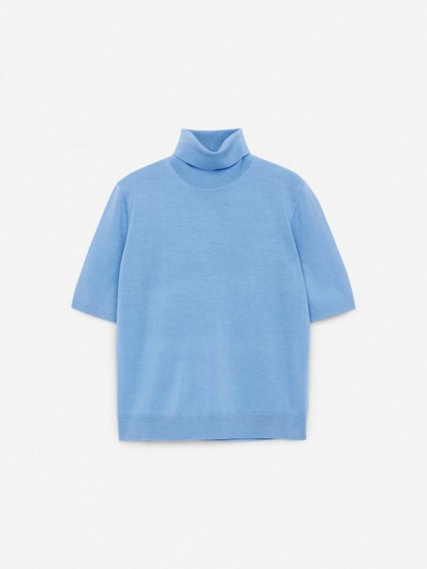 Ein hellblauer Rollkragenpullover mit kurzen Ärmeln liegt auf einem weißen Hintergrund.