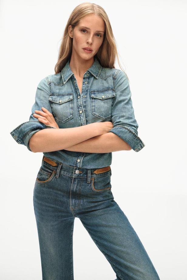 Eine Frau mit blonden Haaren trägt ein Jeanshemd und eine Jeanshose.
