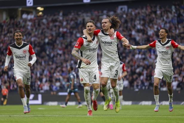Mehrere Fußballspieler von Eintracht Frankfurt jubeln auf dem Rasen vor der Fankurve.