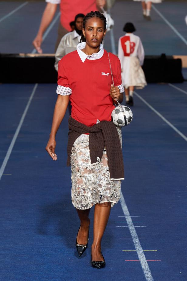 Eine Frau in Sportkleidung mit einer Handtasche in Form eines Fußballs auf einem Laufsteg.