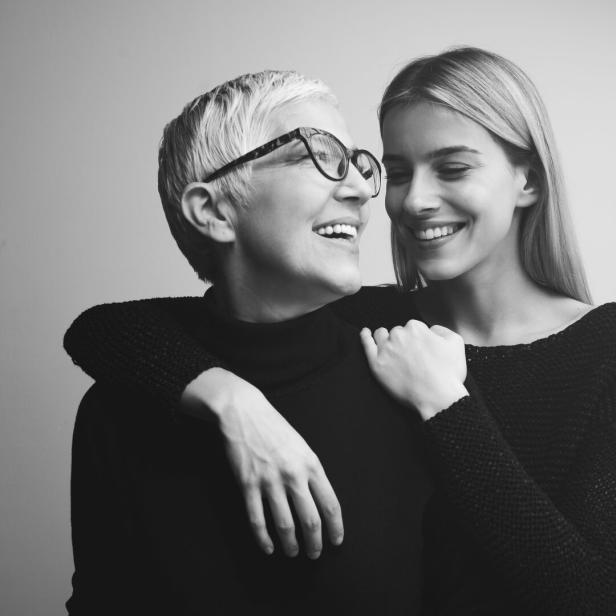 Eine ältere Frau mit Brille umarmt eine jüngere Frau, beide lächeln.