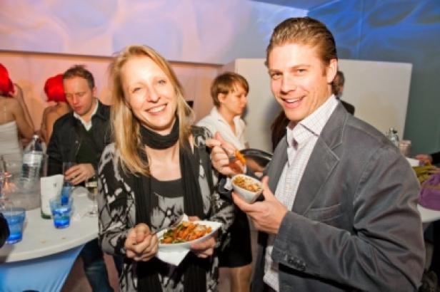 Eine Frau und ein Mann lächeln, während sie auf einer Party asiatisches Essen essen.