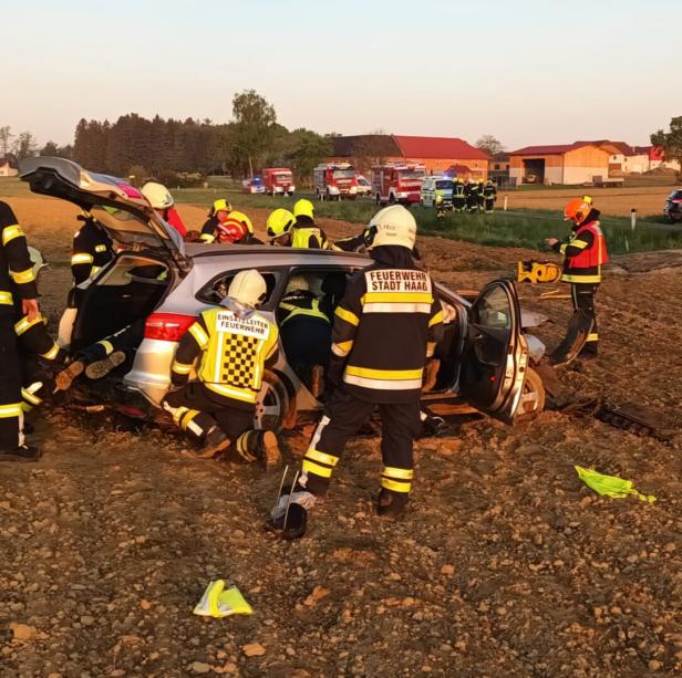Feuerwehrleute der Stadt Haag arbeiten an einem Unfallwagen auf einem Feld.