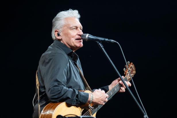 Reinhard Fendrich singt bei einem Konzert und spielt Gitarre.