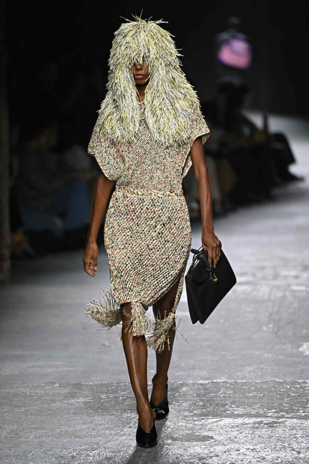 Ein Model mit einem ungewöhnlichen Hut und einem Kleid mit Fransen auf dem Laufsteg von Bottega Veneta.