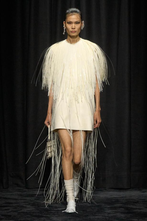 Ein Model präsentiert ein weißes Minikleid mit Fransen und passender Handtasche von Jil Sander.