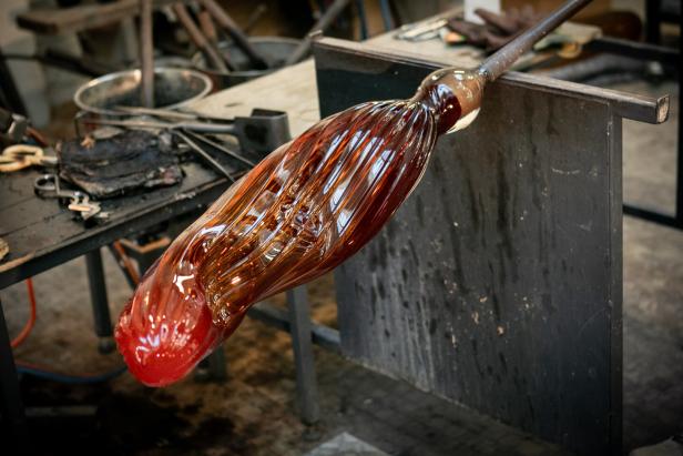 Ein gläsernes, rotbraunes Objekt wird in einer Glasbläserei geformt.
