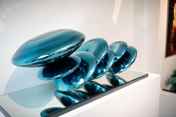 Eine Skulptur aus blauen, linsenförmigen Glaselementen auf einem Spiegelsockel.