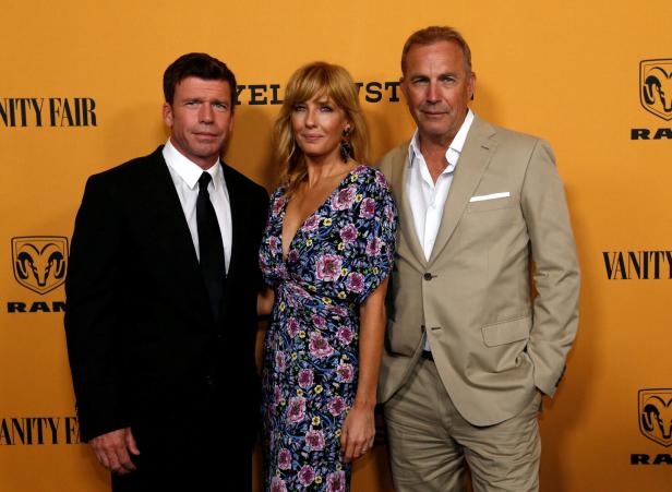 Taylor Sheridan, Kelly Reilly und Kevin Costner posieren auf einem gelben Hintergrund.