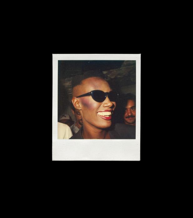 Grace Jones lächelt mit Sonnenbrille auf einem Polaroidfoto.