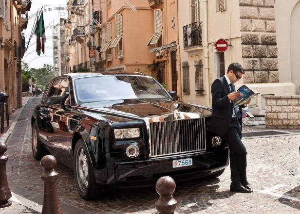 Ein Chauffeur steht an einem Rolls Royce und liest.