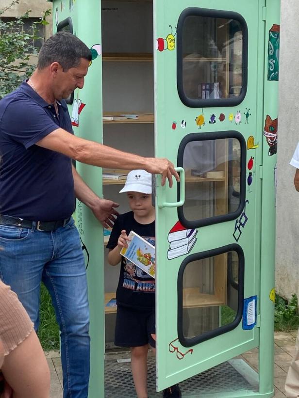 Kind nimmt ein Buch aus einer alten Telefonzelle.