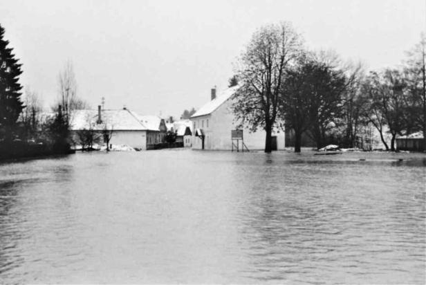 Straßen und Häuser eines Dorfes stehen unter Wasser, Bäume und Dächer sind teilweise von Schnee bedeckt.
