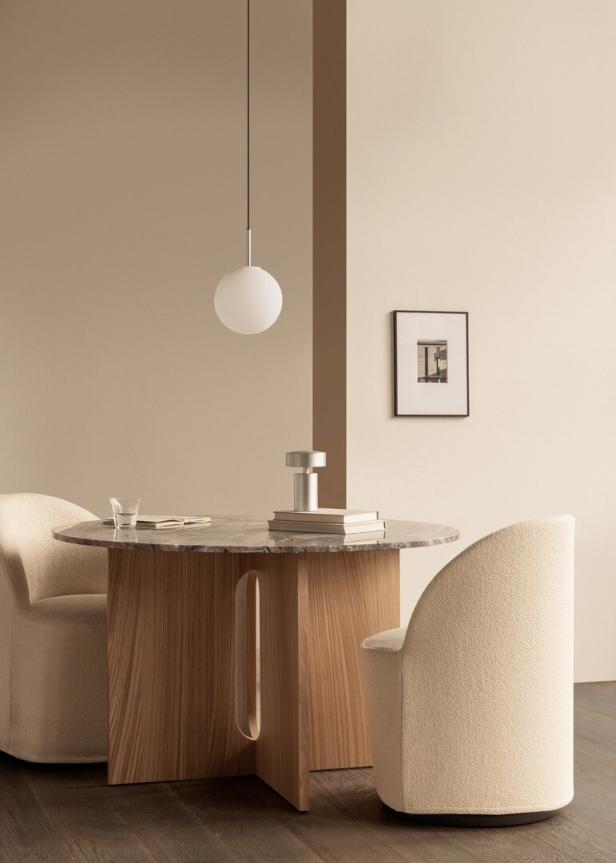 Ein runder Holztisch mit zwei Stühlen und einer Hängelampe in einem minimalistischen Raum.