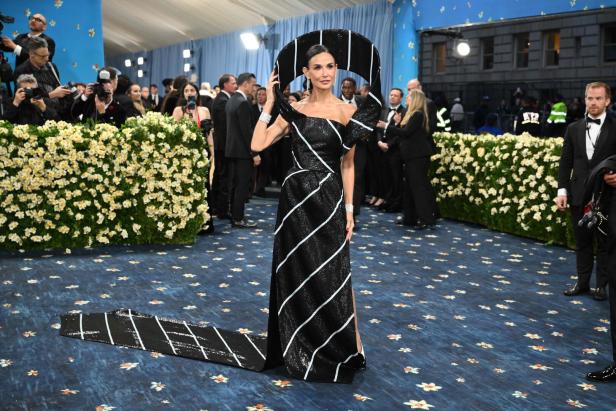 Demi Moore in einem schwarz-weiß gestreiften Kleid und einem übergroßen Hut auf dem roten Teppich der Met Gala.