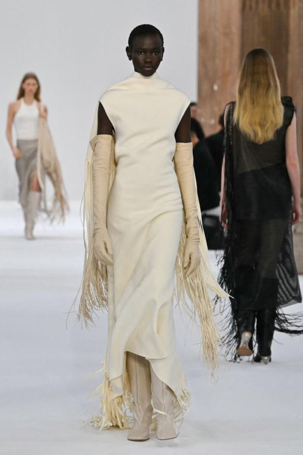 Eine dunkelhäutige Frau präsentiert ein elfenbeinfarbenes Kleid mit Fransen auf dem Laufsteg.