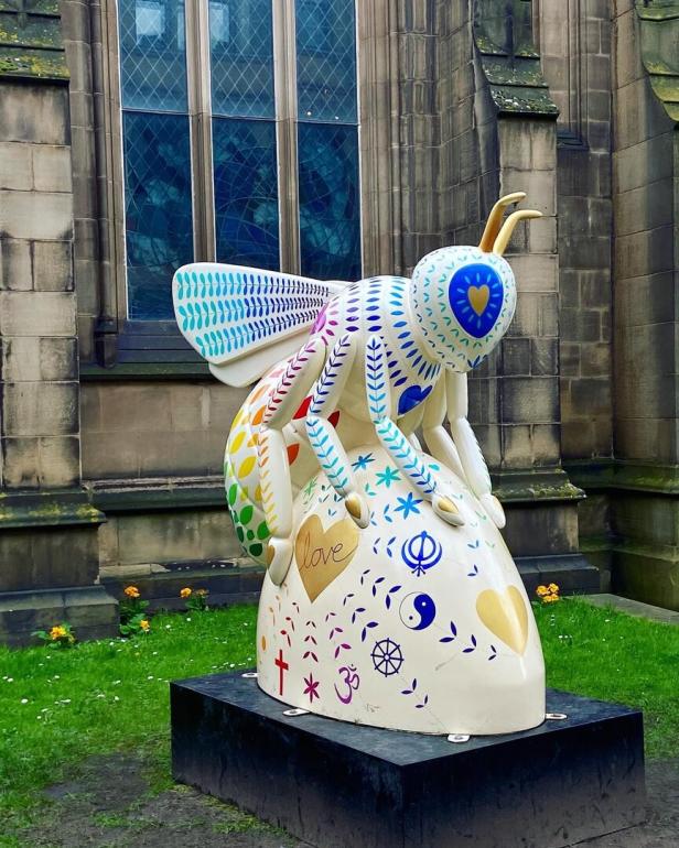 Eine bemalte Bienenstatue steht vor einem Gebäude mit einem großen Fenster.