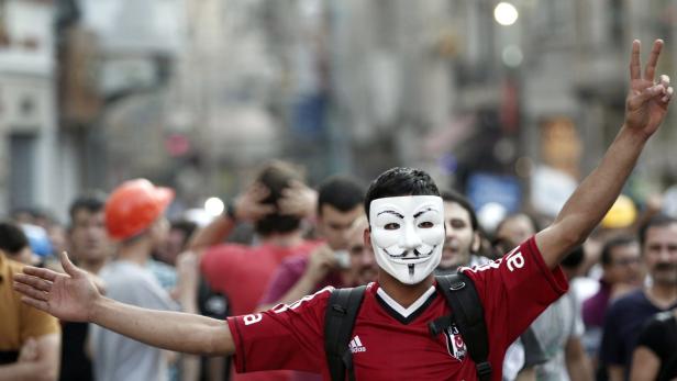 Ein Demonstrant mit Guy-Fawkes-Maske und rotem Trikot inmitten einer Menschenmenge.