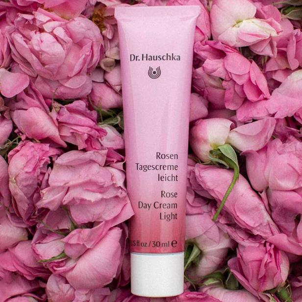 Eine Tube Dr. Hauschka Rosen Tagescreme liegt auf einem Bett aus Rosenblüten.