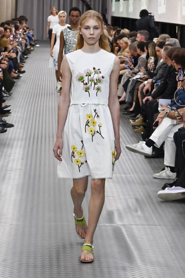 Ein Model präsentiert ein weißes Kleid mit Blumenstickereien auf dem Laufsteg der Miu Miu Spring/Summer 2025 Show.