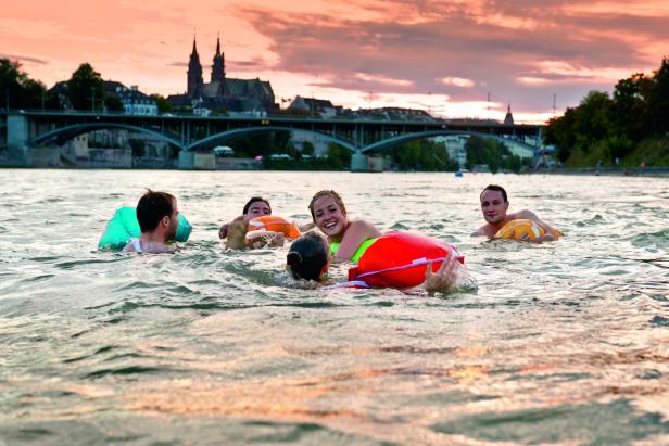 Eine Gruppe von Menschen schwimmt mit Schwimmhilfen im Rhein in Basel.