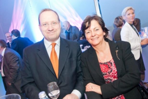 Ein Mann mit Brille und Anzug und eine Frau mit Blazer lächeln in die Kamera.