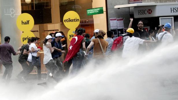 Eine Gruppe von Menschen wird mit einem Wasserwerfer beschossen, einige tragen türkische Flaggen.