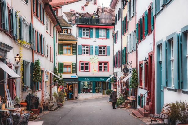 Eine Frau steht in einer Gasse mit bunten Häusern und kleinen Geschäften.