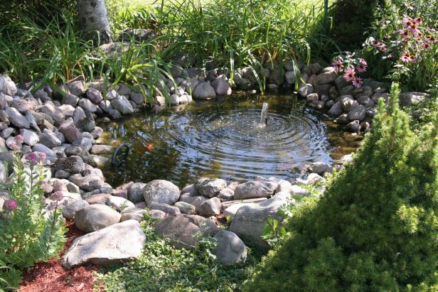 Ein kleiner Teich mit Springbrunnen ist von Steinen und Pflanzen umgeben.