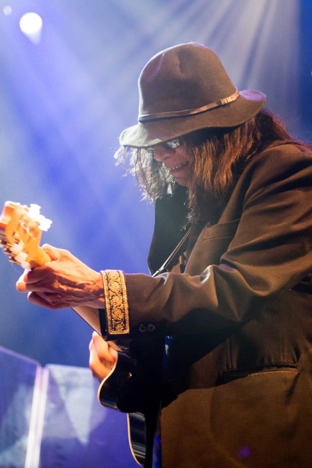 Ein Gitarrist mit Hut und dunkler Brille spielt Gitarre auf einer Bühne.