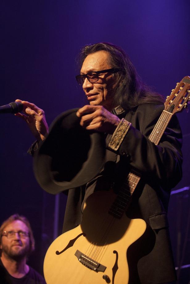 Ein Musiker mit Gitarre hält einen Hut in der Hand.