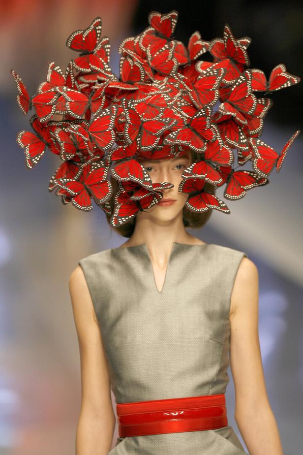 Ein Model mit einem Hut aus roten Schmetterlingen von Alexander McQueen.