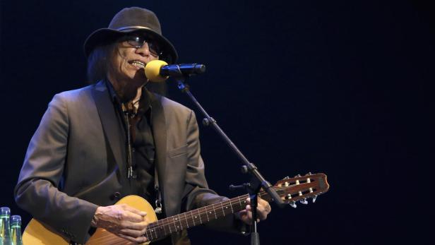 Ein Mann mit Hut und Sonnenbrille spielt Gitarre und singt in ein Mikrofon.