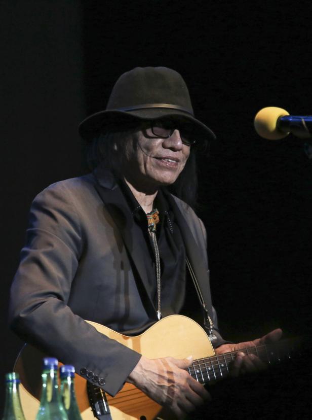 Ein Mann mit Hut und Sonnenbrille spielt Gitarre auf einer Bühne.