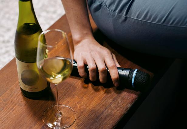 Eine Person hält ein Mikrofon neben einer Flasche Wein und einem mit Wein befüllten Weinglas.