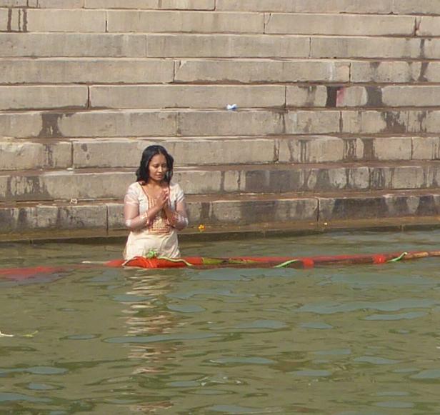 Frau steht betend im Ganges